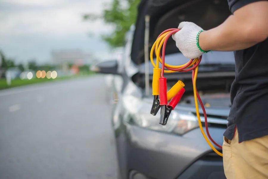 Gloved hands holding jump leads beside a car engine