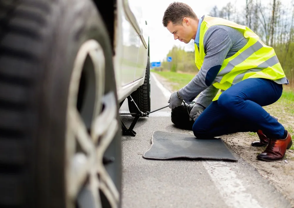Mechanic in a hi-vis vest changing a flat tyre at the roadside