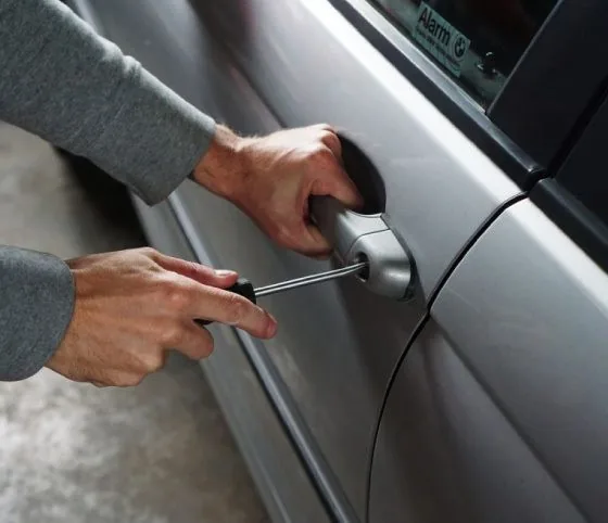 Hands opening a locked car door with a tool