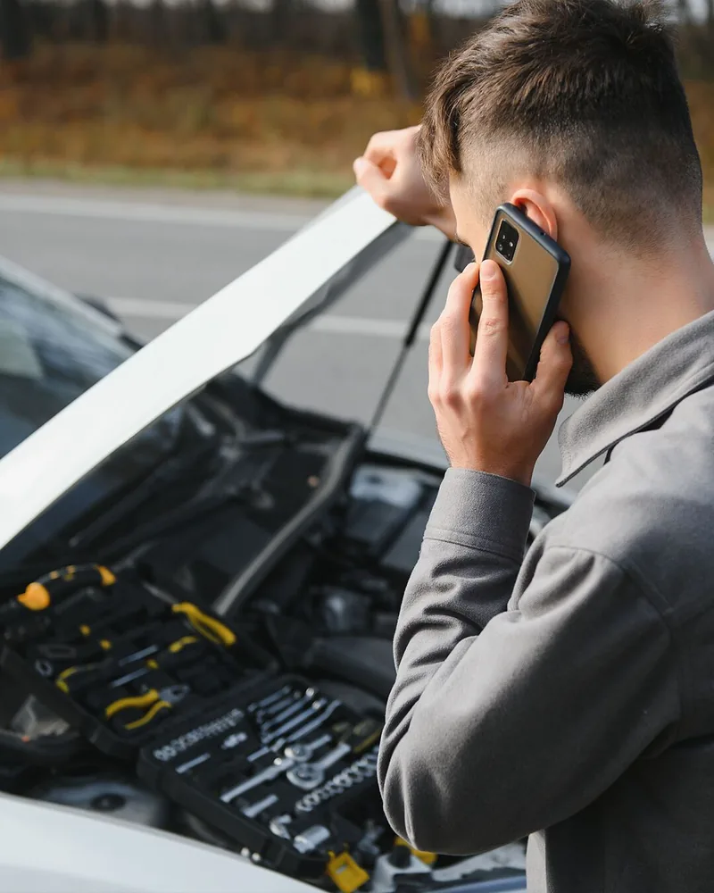 Driver calling for roadside help beside a car with the bonnet up